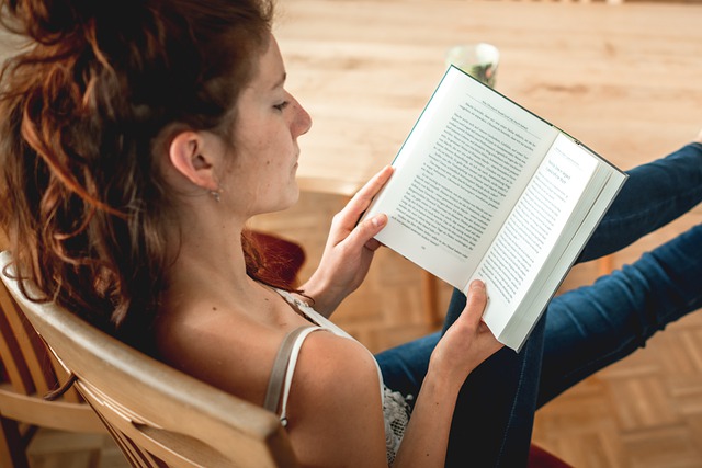 Imagen de una mano mujer joven sentada de espaldas leyendo un libro.