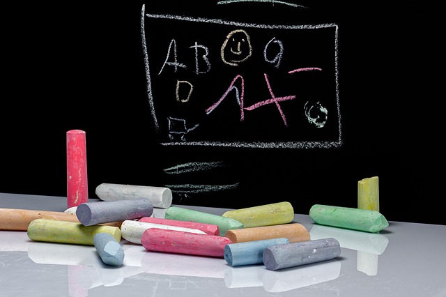 Imagen una mesa blanca con varios crayones de diferentes colores y al fondo un pisaron con letras y números